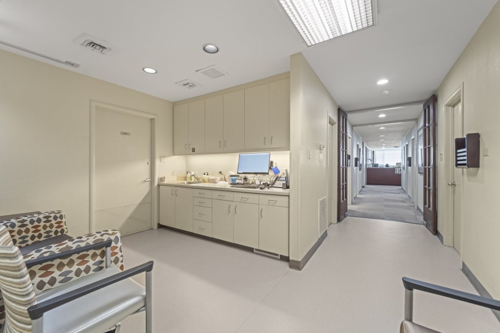 Sterilization/prep area adjacent to hallway: light-colored cabinetry, sink, countertop with equipment, and open corridor leading to treatment rooms