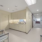 Sterilization/prep area adjacent to hallway: light-colored cabinetry, sink, countertop with equipment, and open corridor leading to treatment rooms