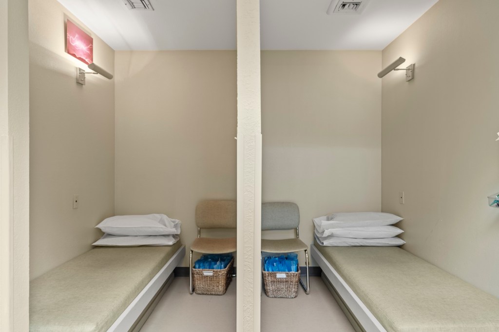 Two private treatment or post-op recovery bays separated by a partition; each contains a cushioned bed, pillow, and storage basket — designed for patient comfort and privacy