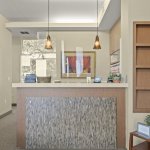 Reception desk with textured stone-like front panel, pendant lighting, framed art on walls, and side shelf with brochures and small plant