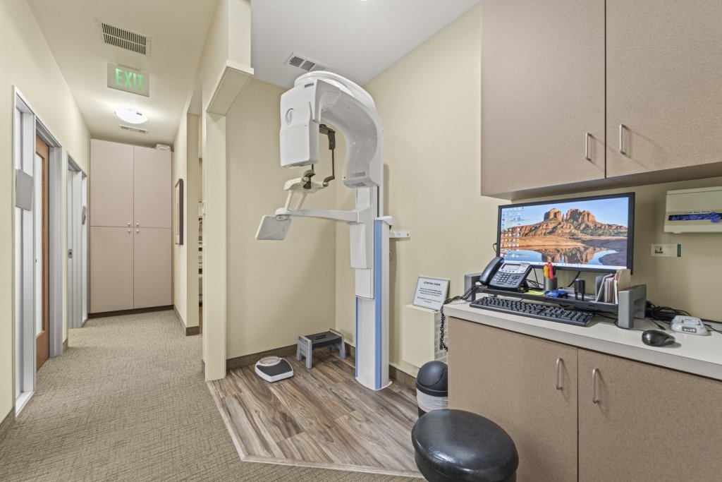 Digital radiography room: upright panoramic X-ray machine, counter with computer monitor displaying dental imagery, storage cabinets, and stool — dedicated for imaging diagnostics